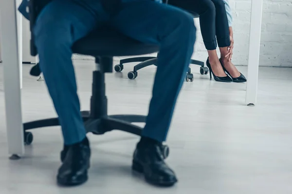 Vista ritagliata di uomo d'affari afro-americano seduto in ufficio vicino al collega che soffre di dolore alla gamba — Foto stock