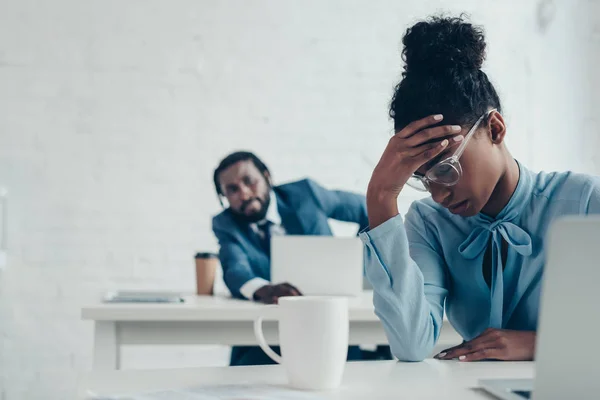 Exhausted businesswoman suffering from headache while sitting in office near colleague — Stock Photo