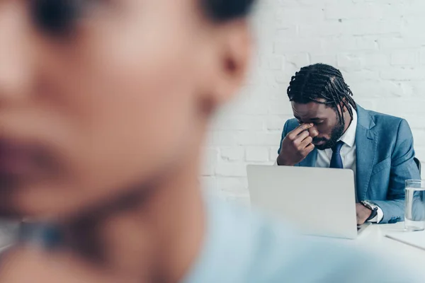 Foco seletivo do gerente americano africano que sofre de dor de cabeça enquanto está sentado no escritório perto do colega — Fotografia de Stock
