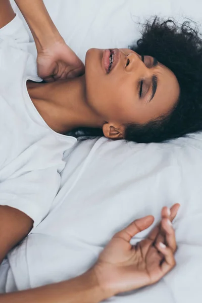 Erschöpfte Afroamerikanerin leidet unter Nackenschmerzen, während sie mit geschlossenen Augen im Bett liegt — Stockfoto