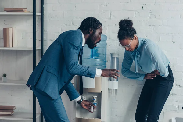 Worried african american manager giving glass of water to pretty colleague suffering from abdominal pain — Stock Photo
