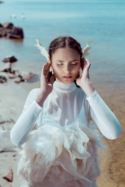 Elegante mujer en traje de cisne blanco cerrando los ojos, tomados de la mano cerca de la cara - foto de stock
