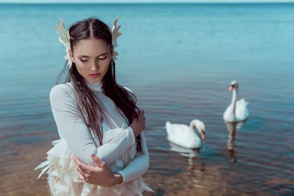 Zarte Frau im weißen Schwanenkostüm schließt die Augen, steht am Fluss mit Vögeln — Stockfoto