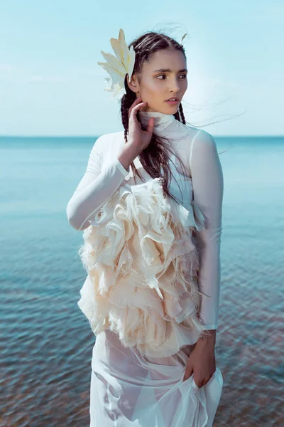 Elegante Frau im weißen Schwanenkostüm steht am Wasser und schaut weg — Stockfoto