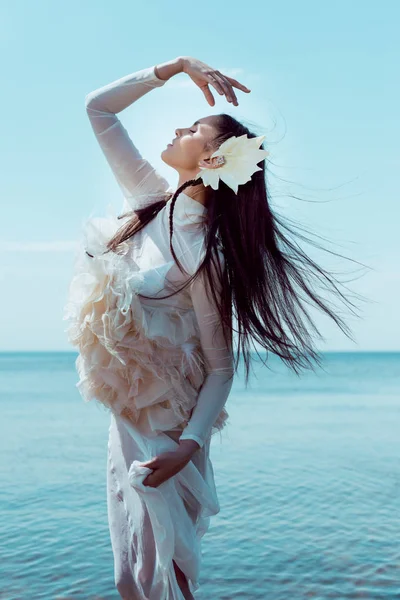 Vista lateral de la mujer joven en traje de cisne blanco haciendo gesto, ojos cerrados - foto de stock