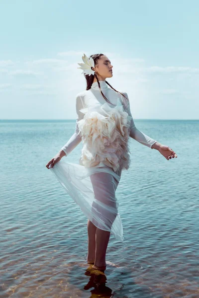 Mujer soñadora y elegante en traje de cisne blanco de pie en el fondo del río - foto de stock