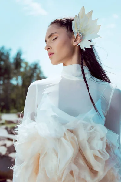 Baixo ângulo vista de mulher macia em traje de cisne branco em pé na floresta e praia fundo — Fotografia de Stock