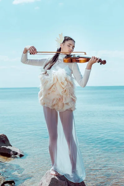 Adult woman in white swan costume with violin playing music on blue river background — Stock Photo