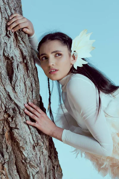 Besorgte erwachsene Frau im weißen Schwanenkostüm steht neben drei Baumstämmen und schaut weg — Stockfoto