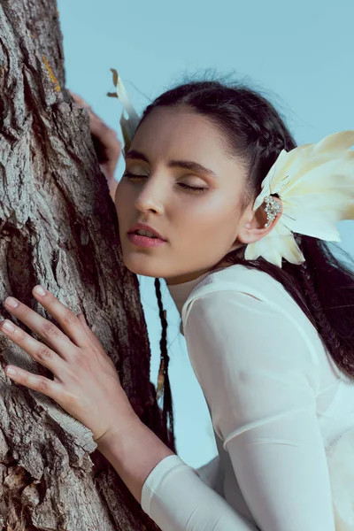 Hermosa mujer en traje de cisne blanco cerrando los ojos, de pie cerca de tres troncos - foto de stock