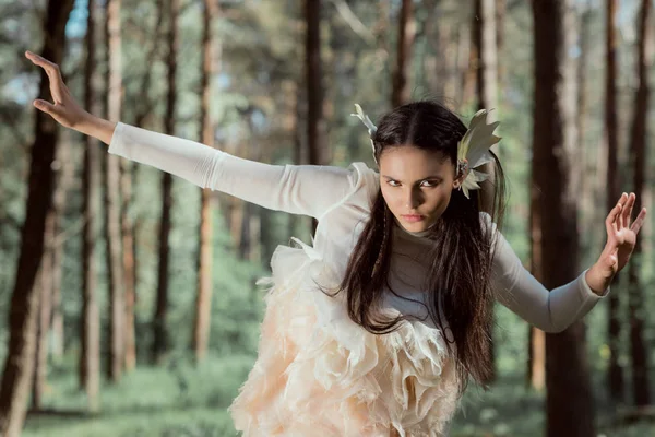 Jovem mulher em traje de cisne branco olhando para longe, de pé na floresta — Fotografia de Stock