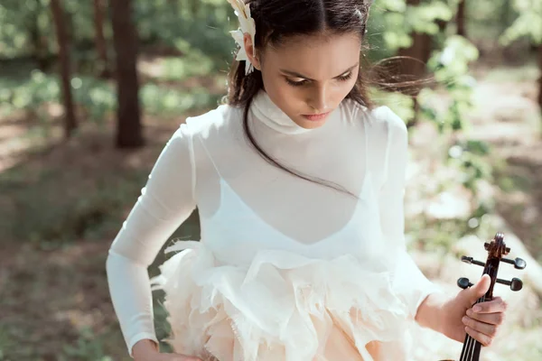 Jeune femme en costume de cygne blanc debout sur fond de forêt avec violon — Photo de stock