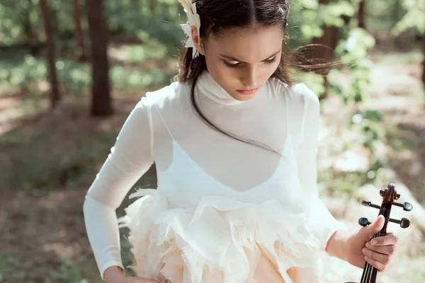 Young woman in white swan costume standing on forest background with violin — Stock Photo