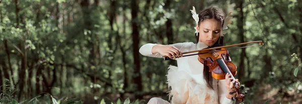 Panoramic view of brunette woman in white swan costume playing on violin — Stock Photo