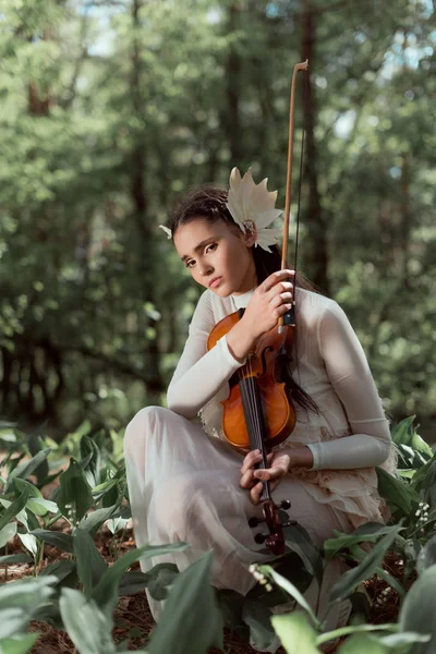 Young woman in white swan costume standing on ground with violin, looking at camera — Stock Photo