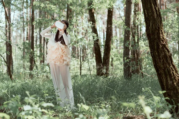 Mujer tierna en traje de cisne blanco y auriculares vr de pie sobre el fondo del bosque - foto de stock