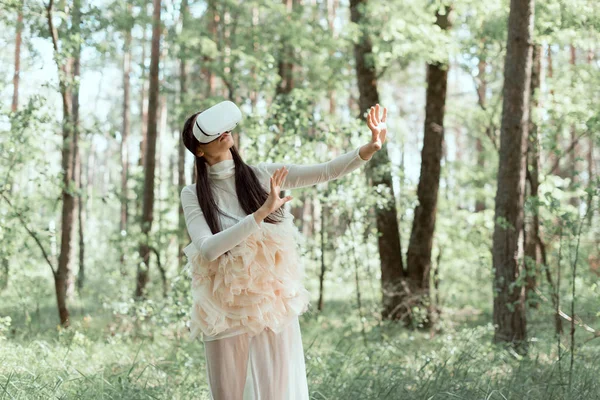 Ніжна жінка в білому лебединому костюмі і гарнітурі vr, що стоїть на лісовому фоні — стокове фото
