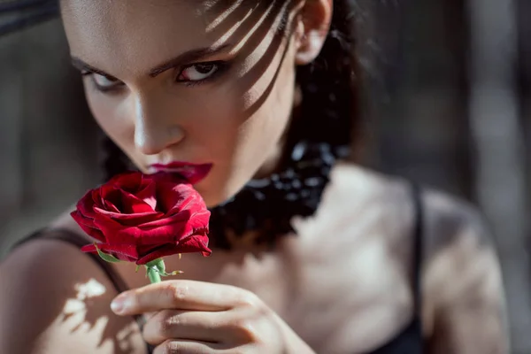 Portrait of beautiful woman in black costume holding red rose in hand, looking at camera — Stock Photo