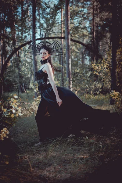 Vue latérale de la femme brune en costume de sorcière debout sur fond de forêt, regardant loin — Photo de stock