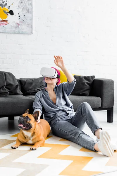 Chica con el pelo colorido y auriculares VR sentado en el suelo cerca del perro - foto de stock