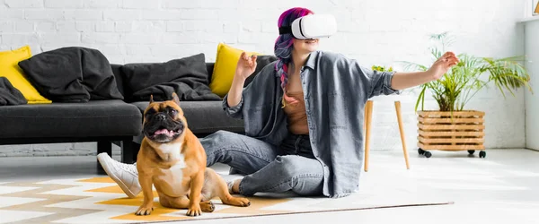 Panoramic shot of girl with colorful hair and VR headset sitting on floor near dog — Stock Photo