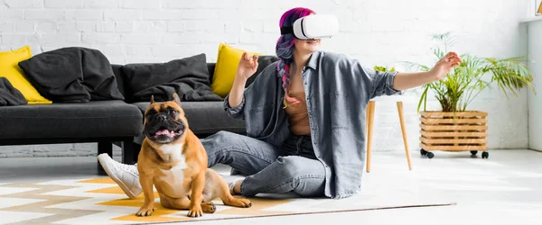 Tiro panorâmico de menina com cabelo colorido e fone de ouvido VR sentado no chão perto do cão — Fotografia de Stock