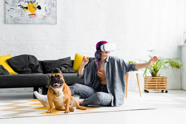 Girl with colorful hair and VR headset gesturing and sitting on floor near dog — Stock Photo