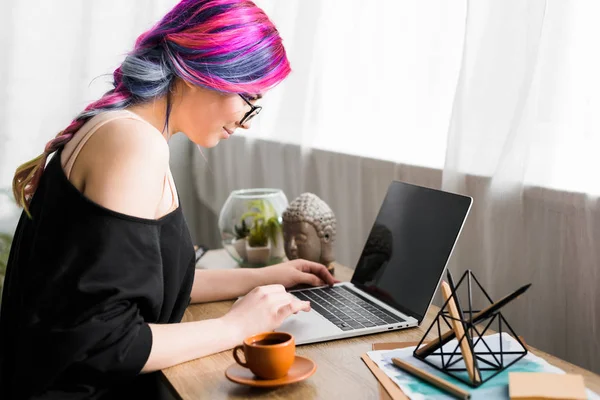 Vista lateral da menina com cabelo colorido sentado na mesa e usando laptop — Fotografia de Stock
