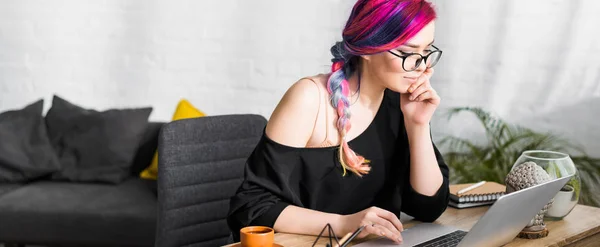 Panoramic shot of girl with colorful hair sitting at desk and using laptop — Stock Photo