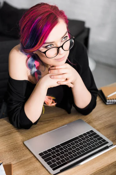 Beautiful girl with colorful hair sitting behind table and looking away — Stock Photo