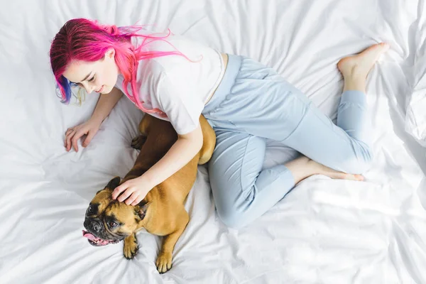 Над головой вид девушки с красочными волосами, играющей с собакой в постели — стоковое фото