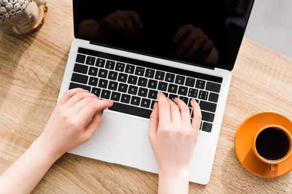 Cropped view of woman using laptop on table near cup of coffee — Stock Photo