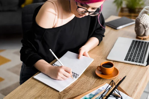 Fille hipster avec des cheveux colorés assis à la table et des notes d'écriture — Photo de stock