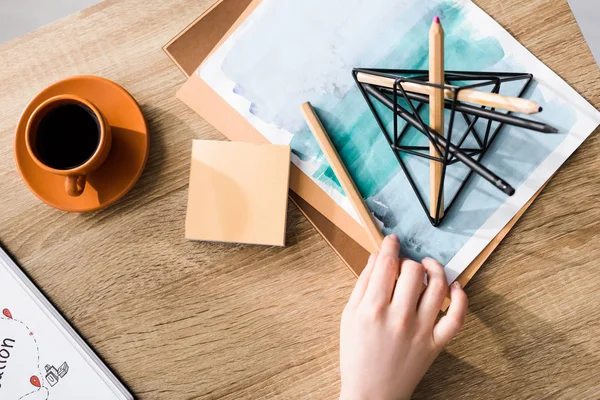 Cropped view of girl holding pencil on table near of cup of coffee, sticky notes, drawing and notebook — Stock Photo