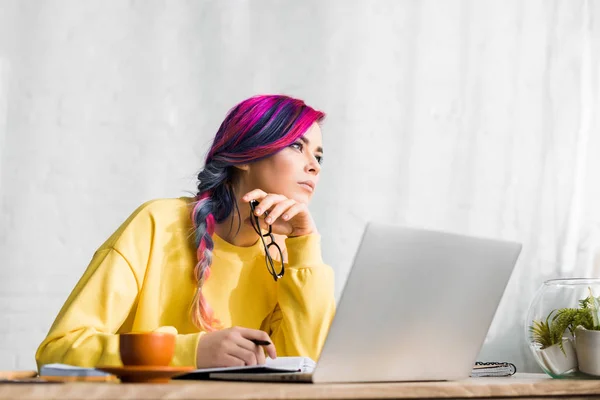 Girl with colorful hair sitting at table and looking away pensively — Stock Photo