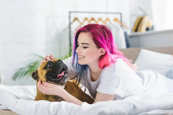 Girl with colorful hair laying in bed with french bulldog — Stock Photo