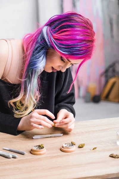 Femme hipster avec des cheveux colorés rouler joint de marijuana médicale tout en étant assis à la table — Photo de stock