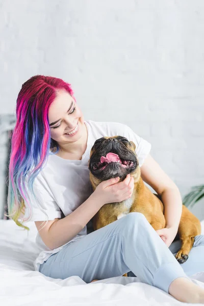 Alegre hipster menina sentado na cama e acariciando francês bulldog — Fotografia de Stock