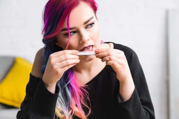 Hermosa chica lamiendo articulación con cannabis medicinal y mirando hacia otro lado - foto de stock