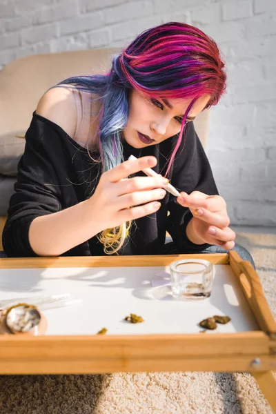 Concentré belle fille faire joint avec de la marijuana médicale tout en étant assis sur le sol derrière la table — Photo de stock
