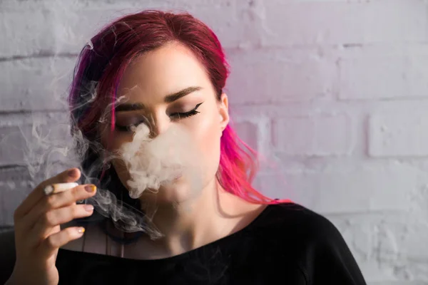 Beautiful girl with colorful hair and closed eyes smoking joint — Stock Photo