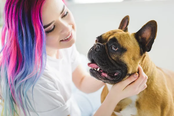 Jolie fille avec des cheveux colorés caressant et regardant mignon bouledogue français — Photo de stock