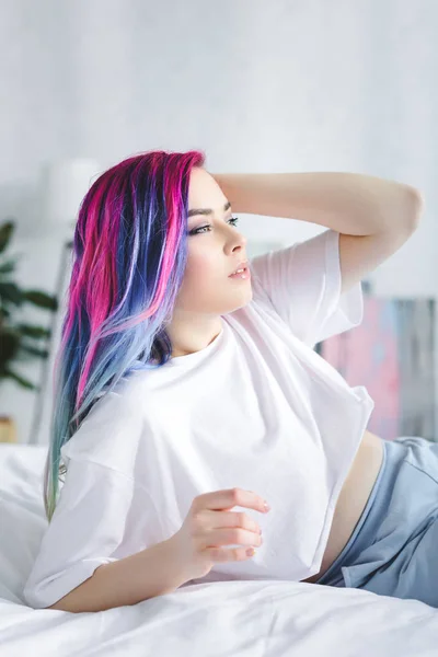 Menina atraente com cabelo colorido deitado na cama e olhando para longe — Fotografia de Stock