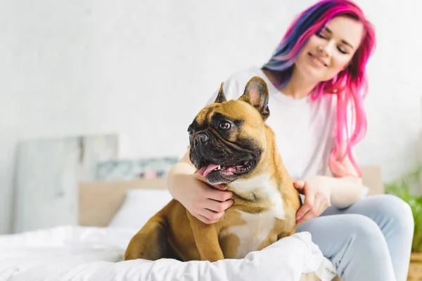 Selective focus of girl sitting on bed and petting cute bulldog looking away — Stock Photo