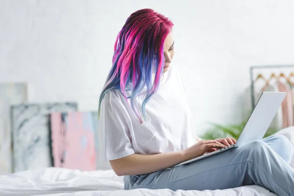 Fille avec des cheveux colorés assis dans le lit et en utilisant un ordinateur portable — Photo de stock