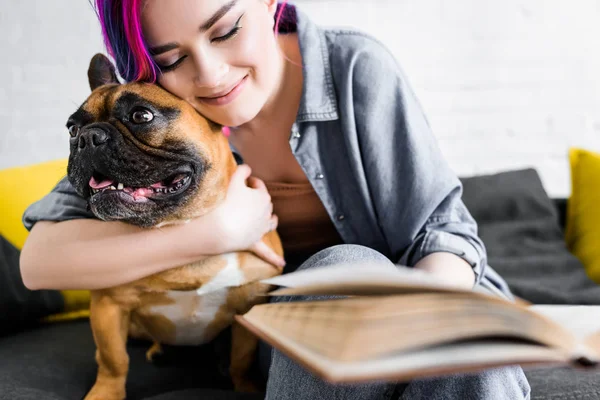 Foco seletivo da menina hipster com cabelo colorido abraçando cão bonito e livro segurando — Fotografia de Stock