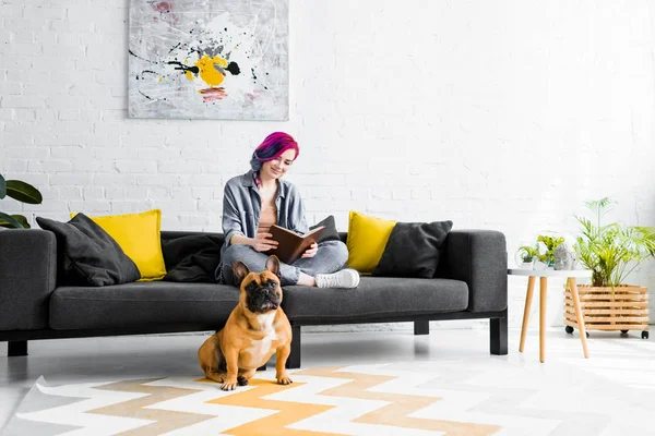Schönes Mädchen sitzt auf Sofa im Wohnzimmer und kleine Bulldogge sitzt auf dem Boden — Stockfoto