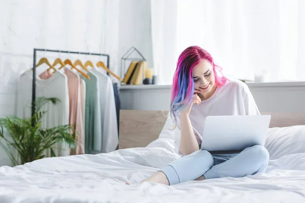 Attraktives Mädchen mit buntem Haar sitzt auf dem Bett und benutzt Laptop — Stockfoto