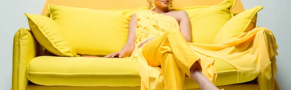 Панорамний знімок молодої жінки, що сидить на жовтому дивані на білому — стокове фото