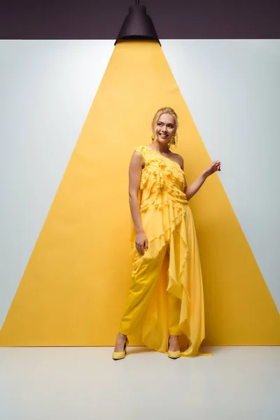 Glückliches blondes Mädchen lächelt, während es auf weiß-gelb posiert und gestikuliert — Stockfoto